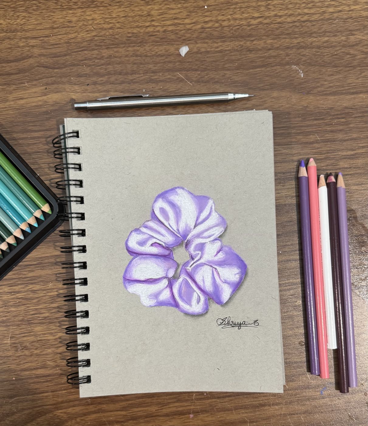 Coloured-pencil drawing of a purple scrunchie in a sketchbook, pencils alongside.