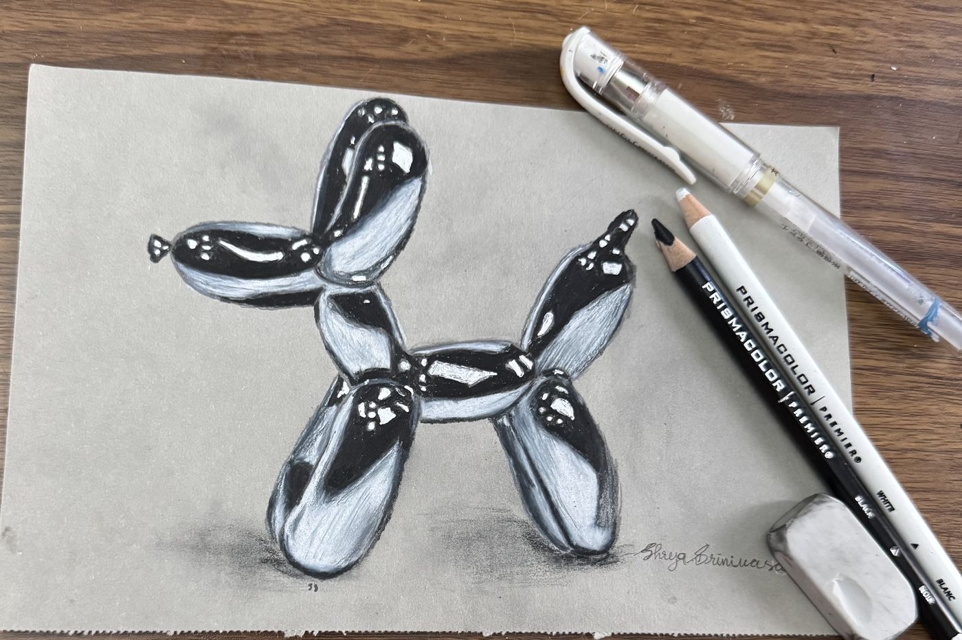 Graphite drawing of a balloon dog, pens and eraser alongside.